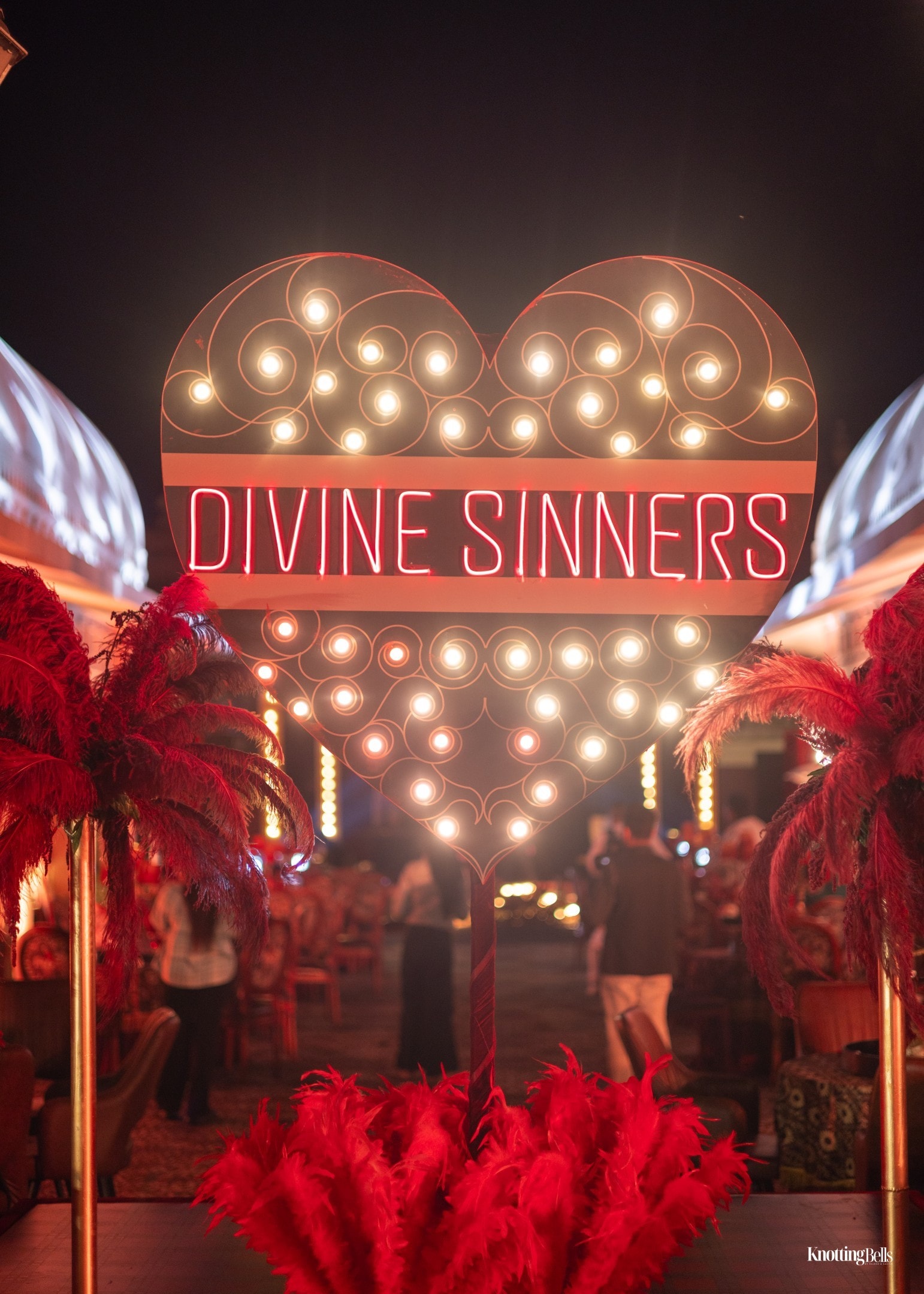 Divine Sinners illuminated heart marquee sign with red feathers at night